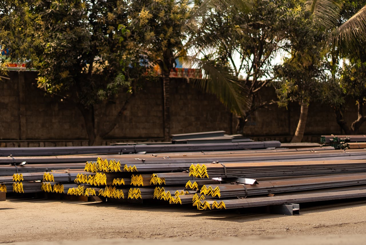 Stacked steel bars in an outdoor industrial area with trees providing a natural backdrop.
